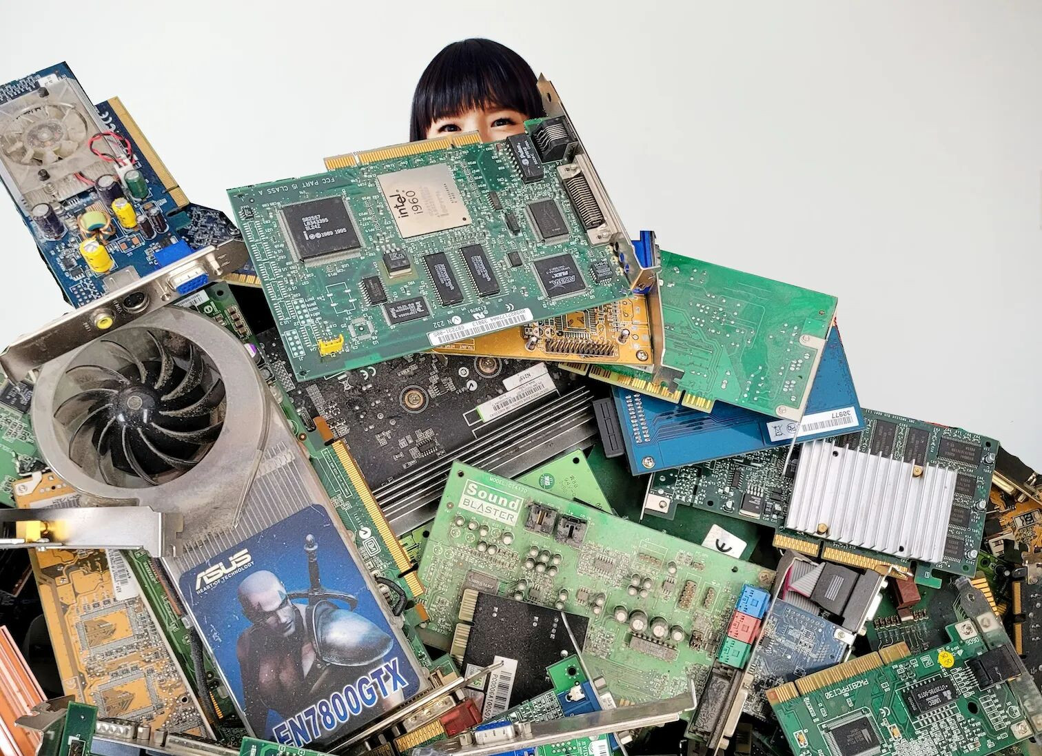 Stack of old PC components like graphics or sound cards, behind it
barely visible (eyes and upwards) the head of Marie Kondo, Japanese
clean up
specalist.